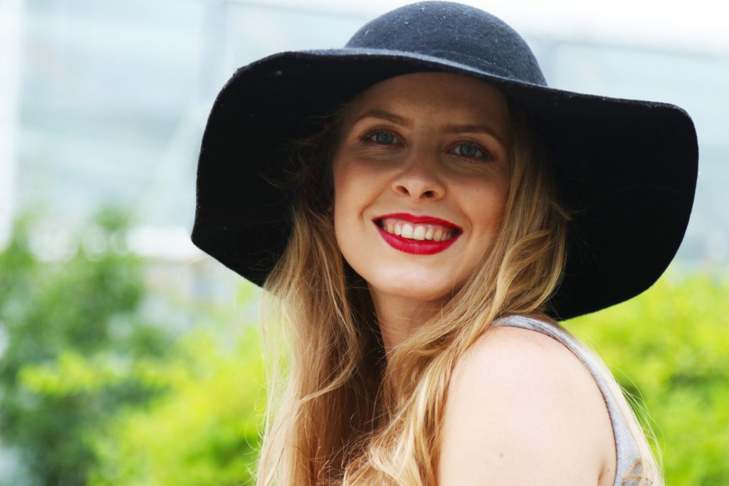 Lachend, junge Frau, mit langen blonden Haaren und schwarzem Hut.