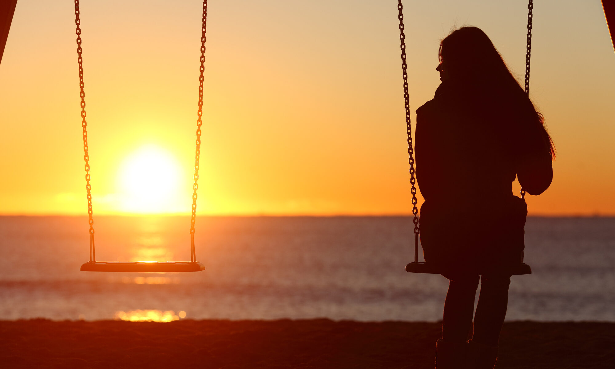 Frau sitzt alleine voller Sehnsucht auf einer Schaukel im Sonnenuntergang